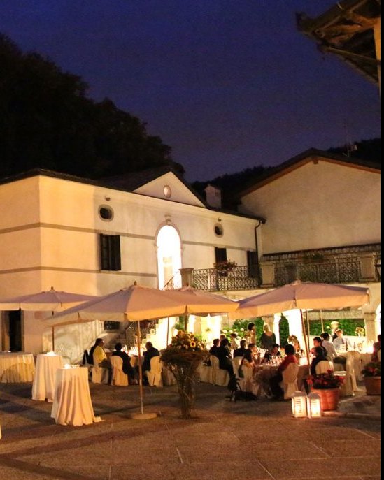Una cena di festa sotto gli ombrelloni nel cortile illuminato di Palazzo Scolari, di sera